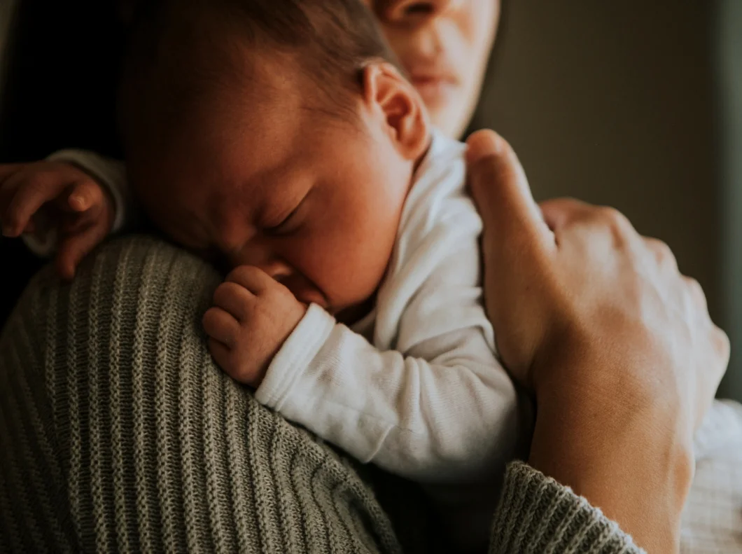 Nahaufnahme eines schlafenden Neugeborenen, das geborgen auf der Schulter einer Bezugsperson liegt.